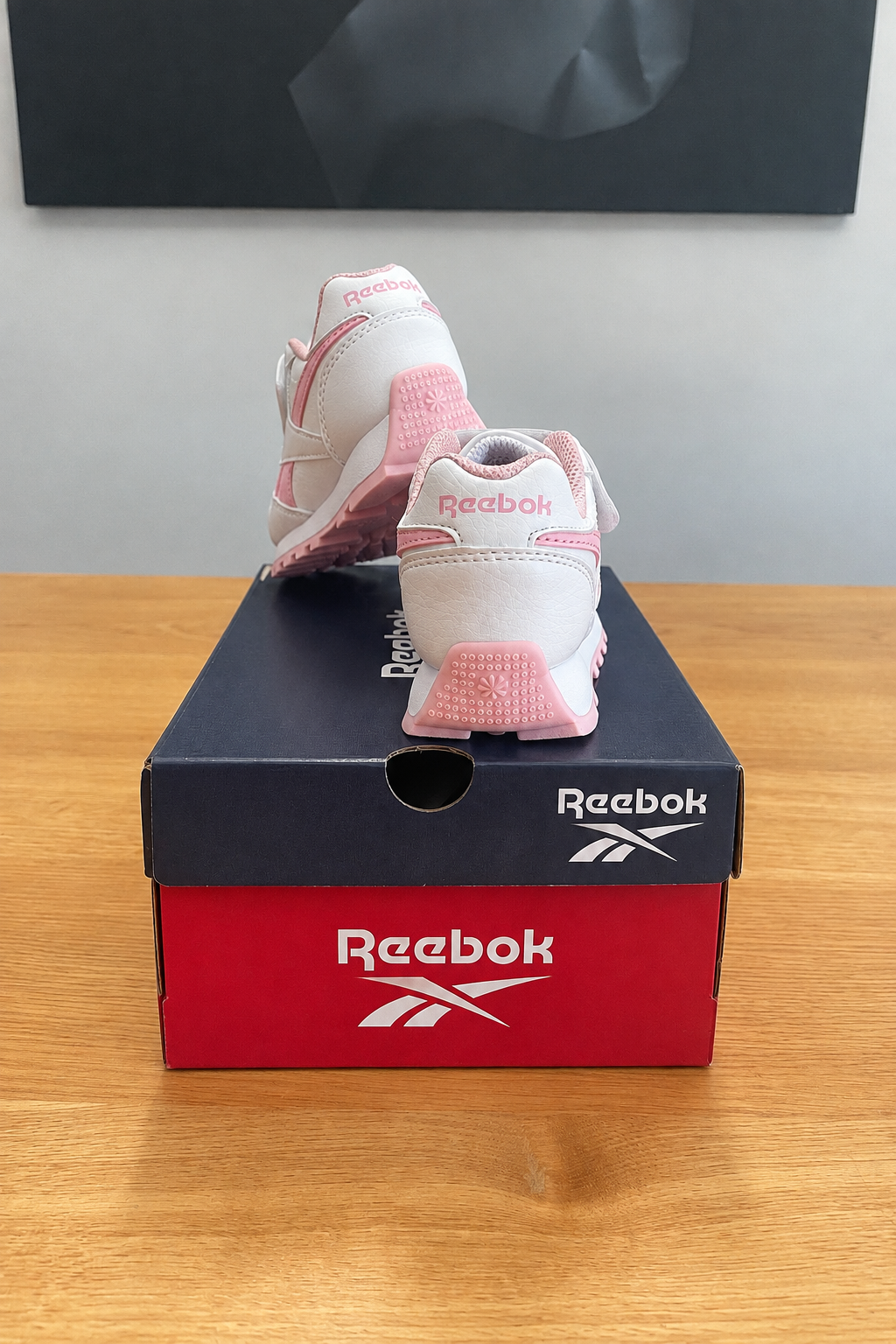 Version retouchée générée de la deuxième photo : vue arrière conservée, boîte sans étiquette et logo Reebok stylisé, recentrée sous le tableau noir