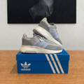 Adidas Retropy F2 W grises et bleu clair sur boîte centrée sous tableau, photo retouchée