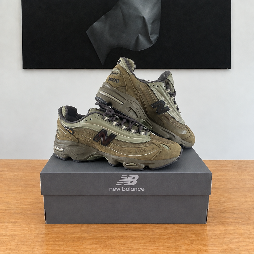 New Balance M1000 NBU : boîte et chaussures centrées sous le tableau noir, avec logo New Balance