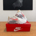 Nike Air Max Excee blanches et rose corail sur boîte rouge centrée, photo retouchée