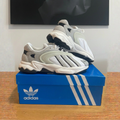 Adidas Oztral W blanches et grises sur boîte bleue centrée, photo retouchée