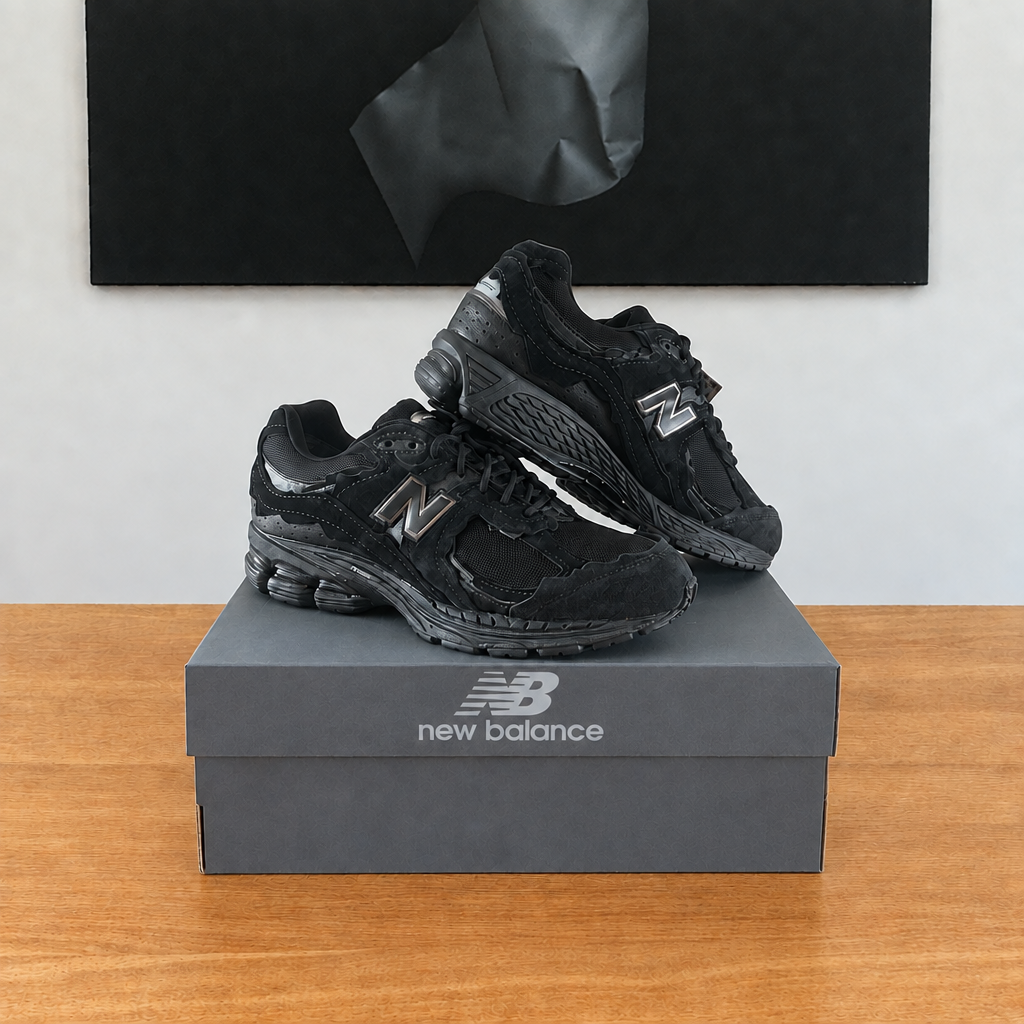 New Balance U2002 : boîte et chaussures centrées sous le tableau noir, avec logo New Balance, boîte réparée en bas à droite