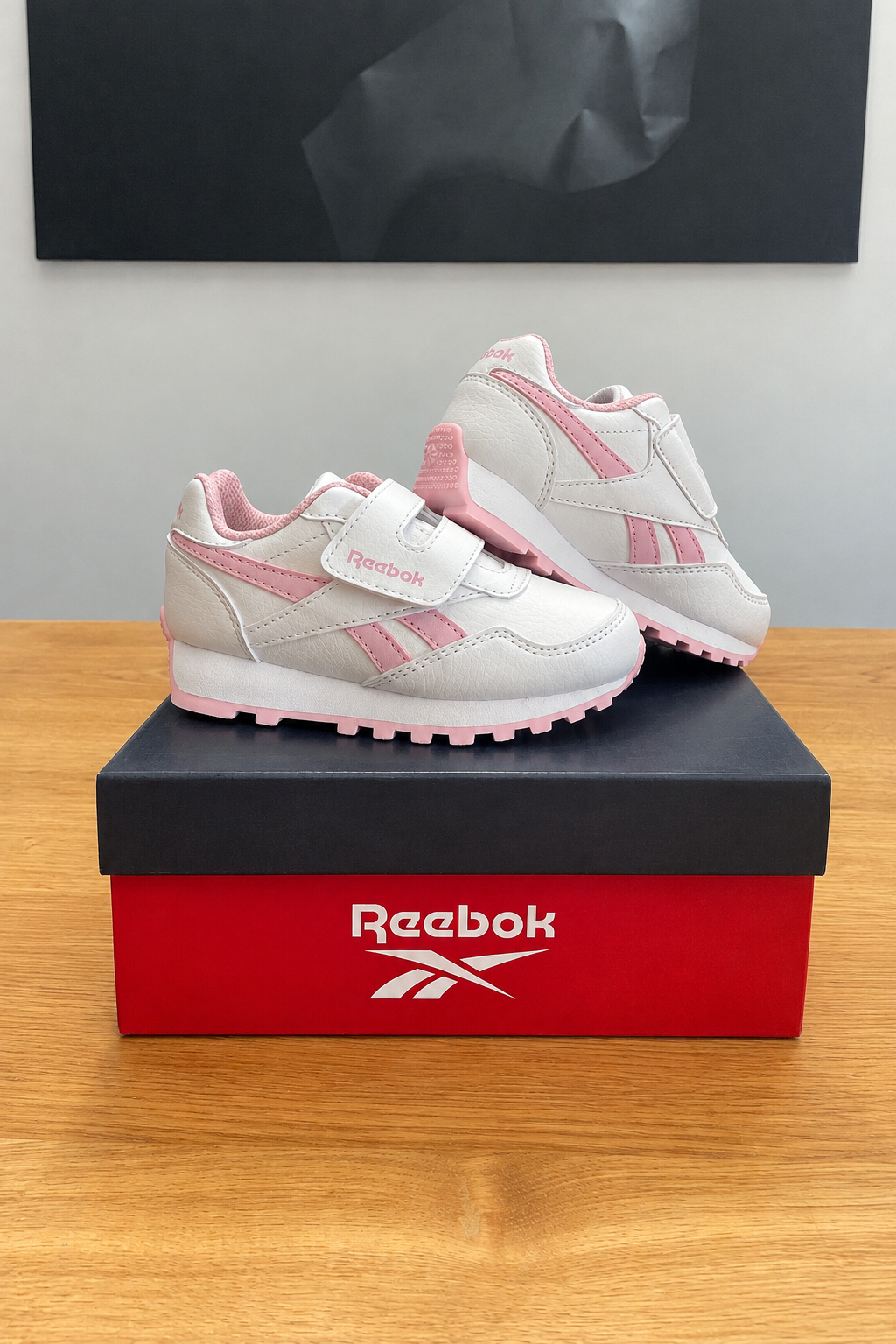 Version retouchée générée de la première photo : boîte Reebok centrée sous le tableau noir, logo stylisé fidèle à l’original
