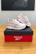 Version retouchée générée de la première photo : boîte Reebok centrée sous le tableau noir, logo stylisé fidèle à l’original