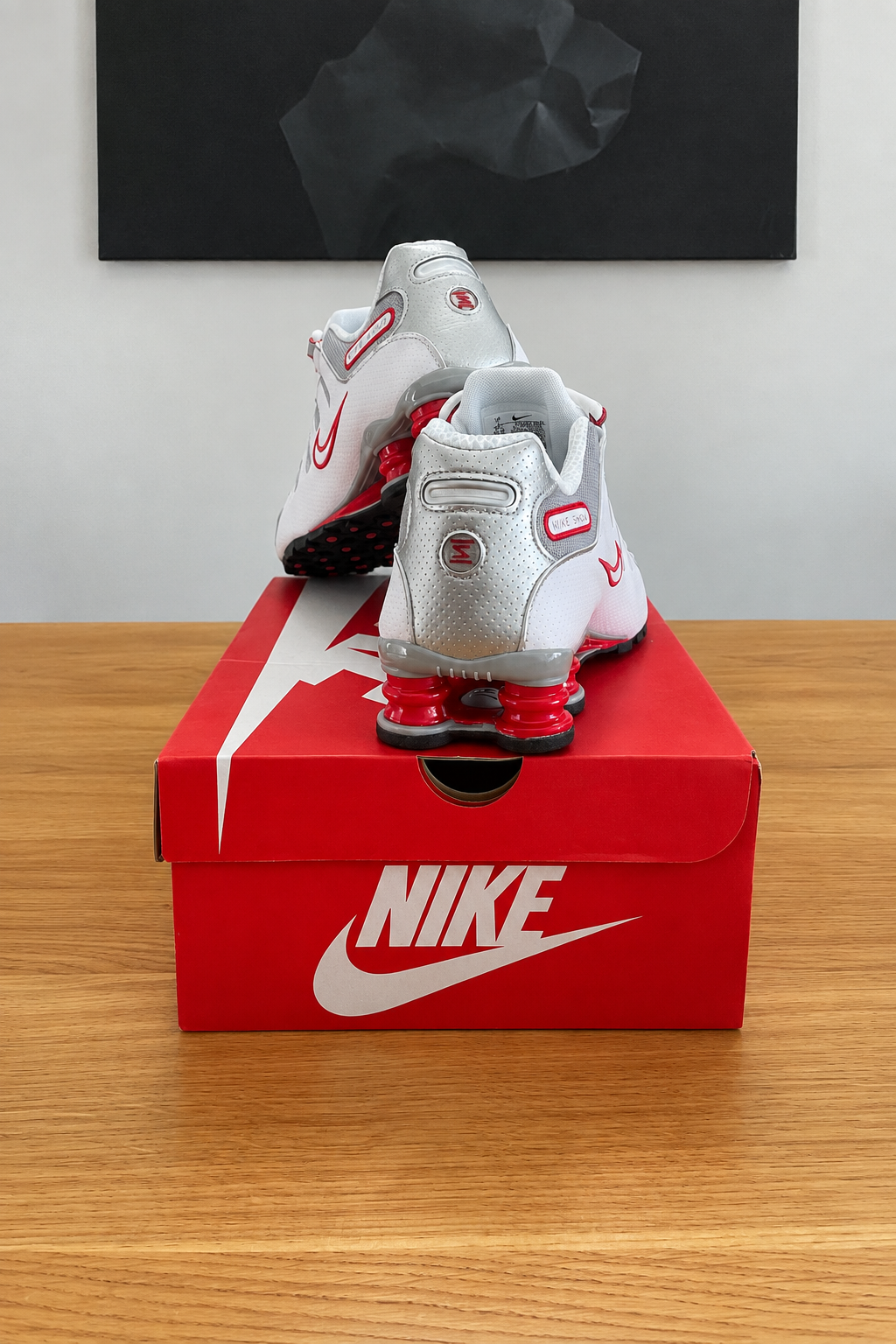 Version retouchée générée de la deuxième photo des Nike Shox NZ : boîte rouge NIKE centrée sous le tableau noir